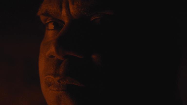 Close-up of a face lit by warm amber light against dark background.