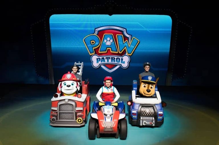 Three Paw Patrol character vehicles displayed on stage beneath illuminated Paw Patrol branding.
