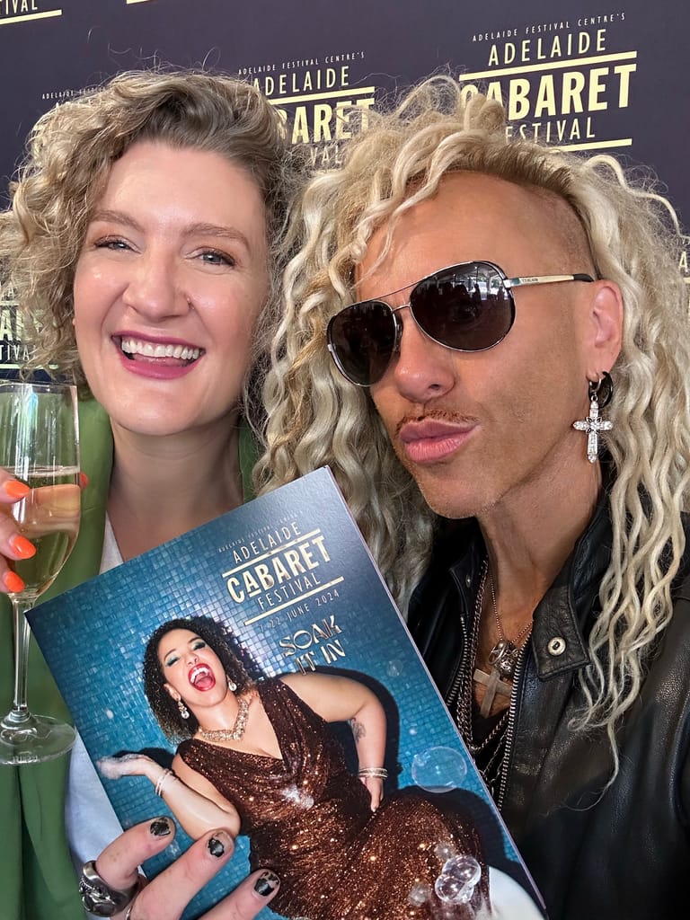 Two people at Adelaide Cabaret Festival event hold programme featuring performer in bronze sequins against blue background.