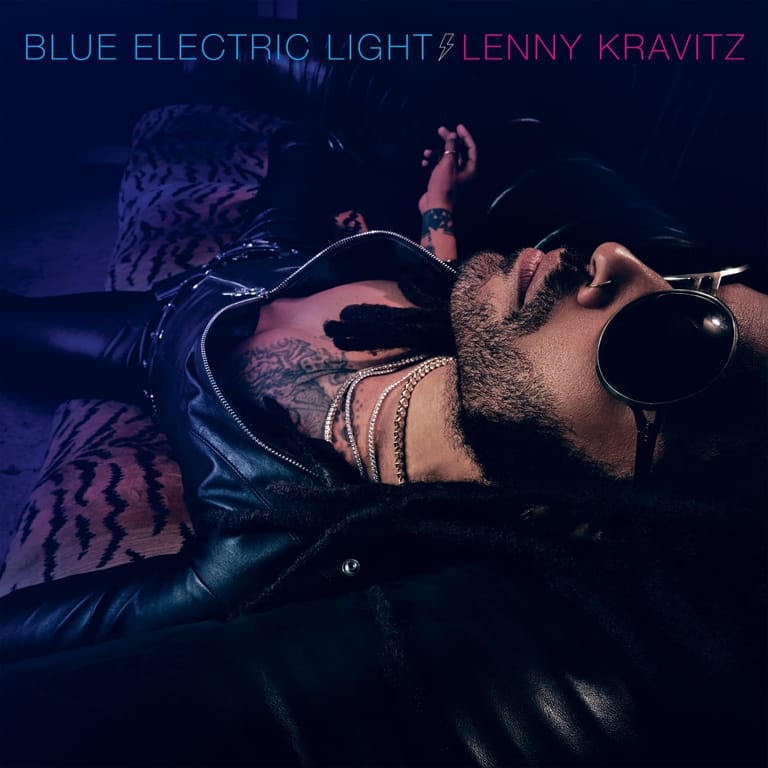 Tattooed performer singing into microphone under blue and pink stage lighting.