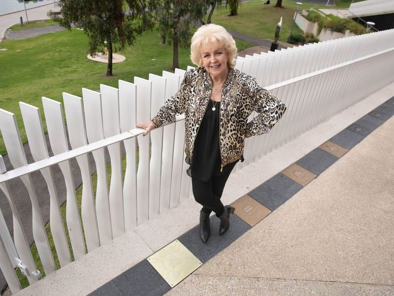 Woman in leopard-print jacket standing beside white curved fence on paved pathway.