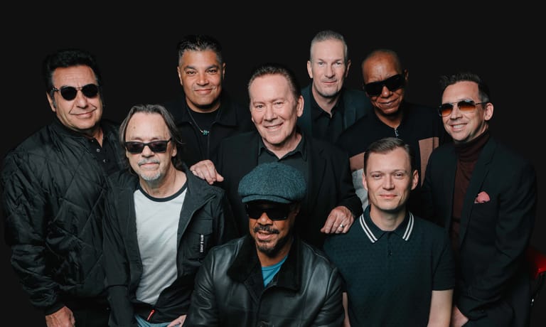 Eight men in dark clothing posed together against a black background in a group portrait.