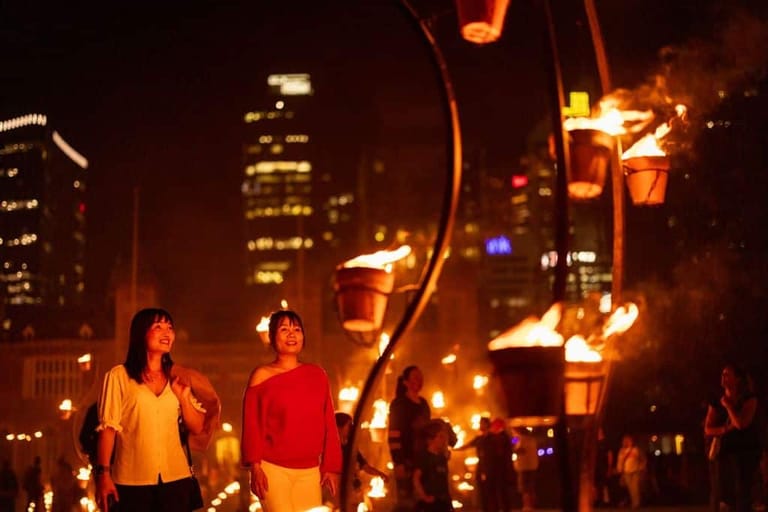 People gather in a city street at night illuminated by glowing lanterns and tall buildings.