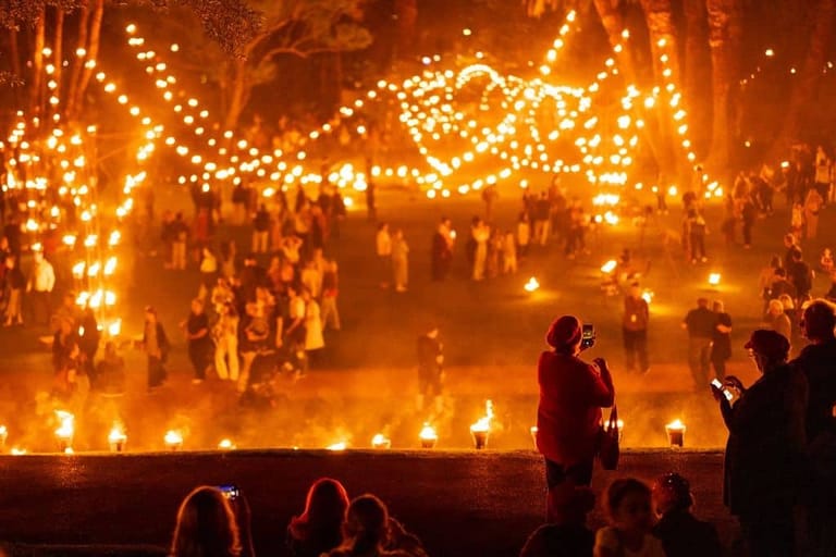 Crowd gathered before a large illuminated structure draped in golden lights at night.