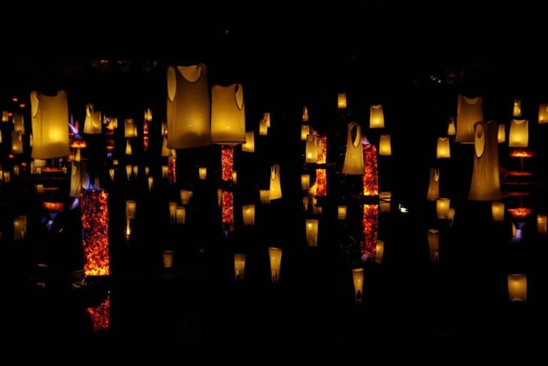 Hundreds of glowing paper lanterns illuminate a dark space in warm gold and amber tones.