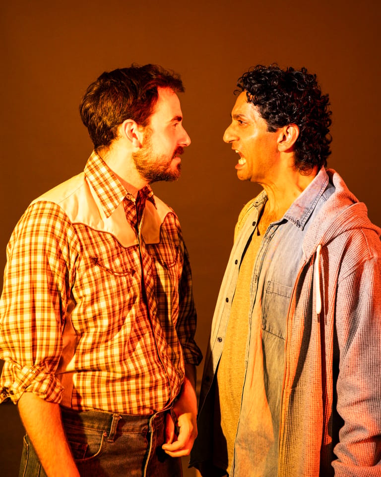Two men in casual shirts face each other against a warm orange backdrop, engaged in conversation.