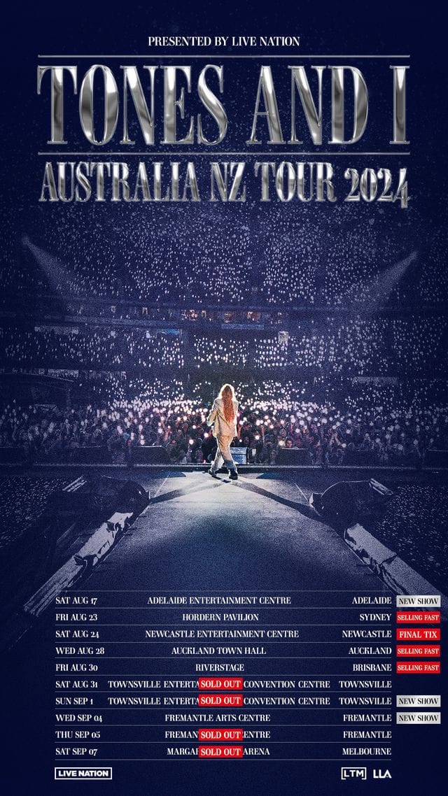Solitary performer on stage illuminated by spotlight, facing thousands of audience members holding phone lights during a large arena concert.