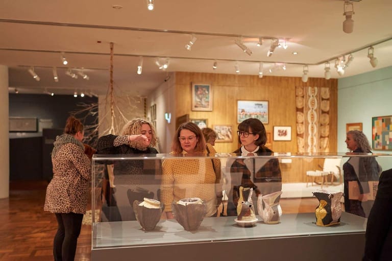Visitors examine jewellery and artefacts displayed in glass cases within a warm-toned museum gallery space.