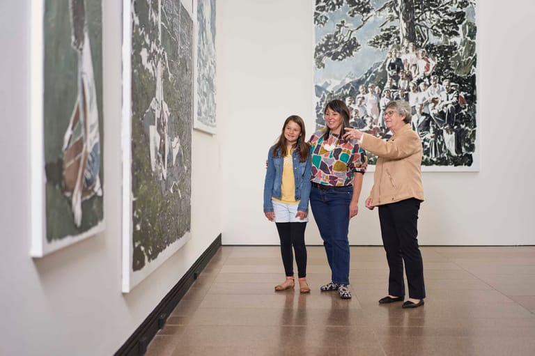 Three visitors examine large monochrome photographs displayed on white gallery walls in a contemporary art space.