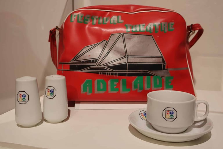 Red branded merchandise bag displayed with white ceramic mugs and saucers featuring matching logo.