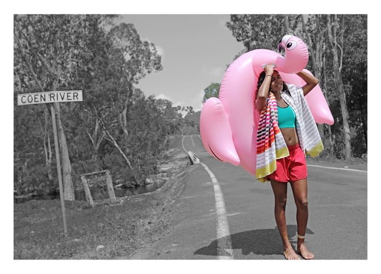 Person holding a large pink inflatable pool float on a rural road near a street sign.
