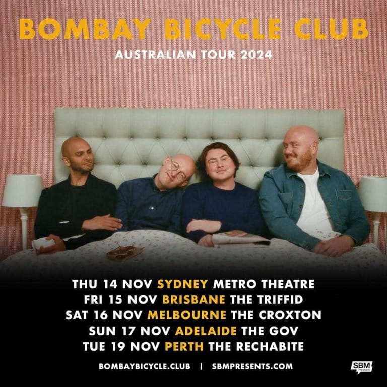 Four band members lounging on a pale green sofa against a textured pink wall, relaxed and posed for the Bombay Bicycle Club Australian tour 2024.