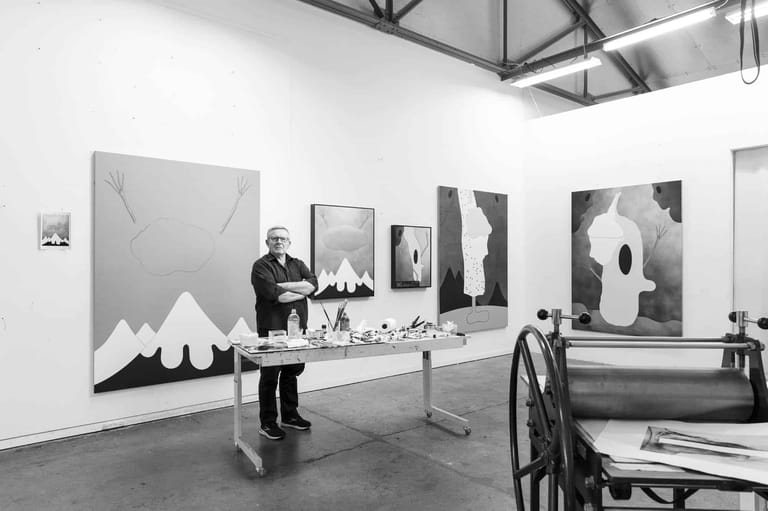 Gallery space with abstract black and white artworks on walls, visitor viewing large mountainous canvas, industrial ceiling.