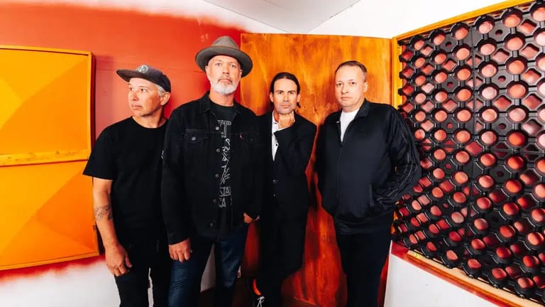Four band members stand against a vibrant orange and red gallery wall installation.