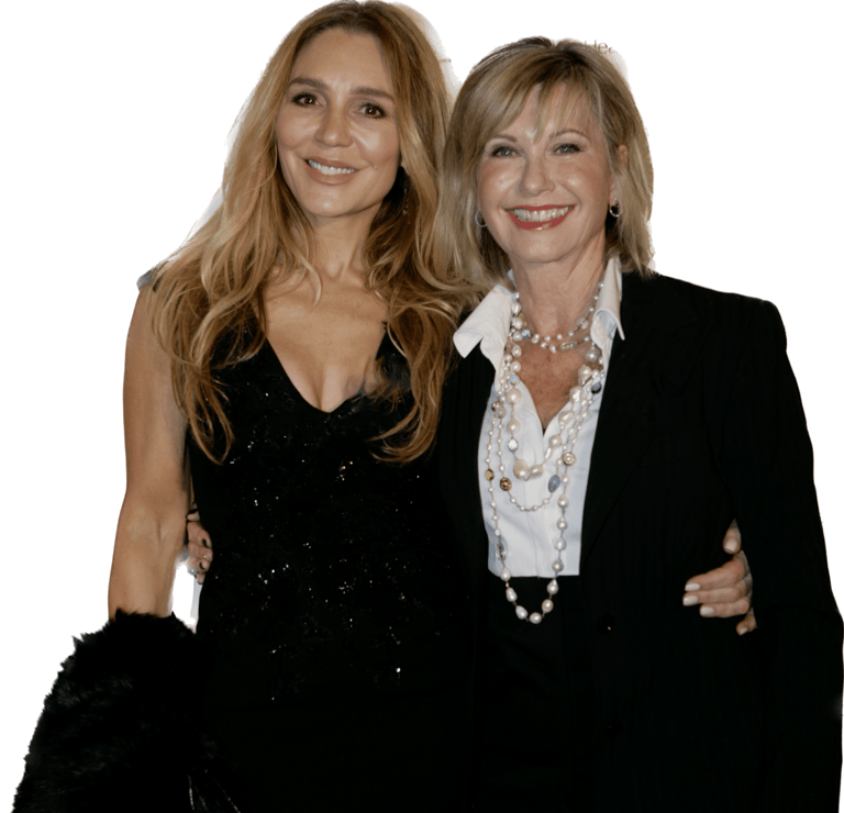Two women pose together smiling, one in a black sequined dress and one in a black blazer with white shirt.