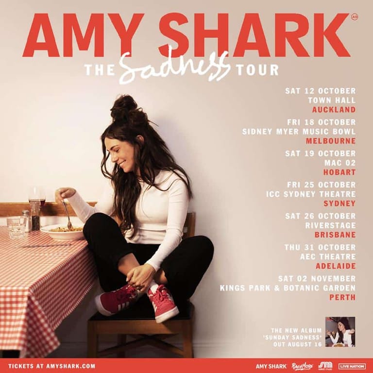 Amy Shark sits cross-legged on a checked floor, looking downward in a contemplative pose, with tour dates listed beside her.