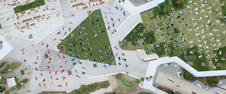 Aerial view of a public space with visitors scattered across manicured lawns and paved areas beside white buildings.