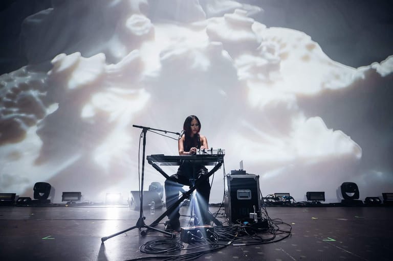 Musician seated at keyboard beneath dramatic clouded sky during outdoor performance.