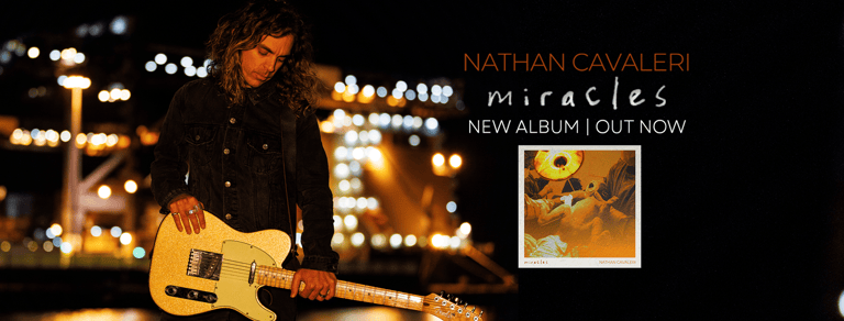 Musician holding yellow acoustic guitar against blurred warm-lit urban nighttime backdrop with album artwork displayed.