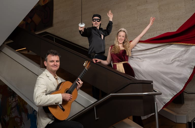 Four musicians pose with guitar, piano and raised arms beside flowing red fabric.