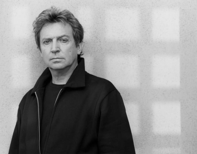 Man in black jacket against neutral textured background, direct gaze, monochrome portrait.