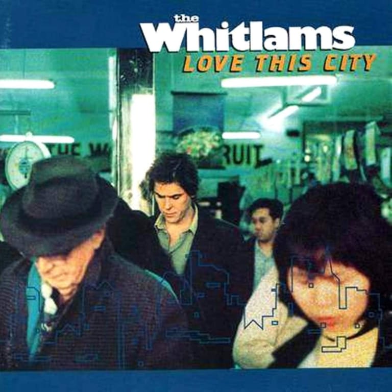 The Whitlams band members posed together in an urban setting with neon signage visible in the background.