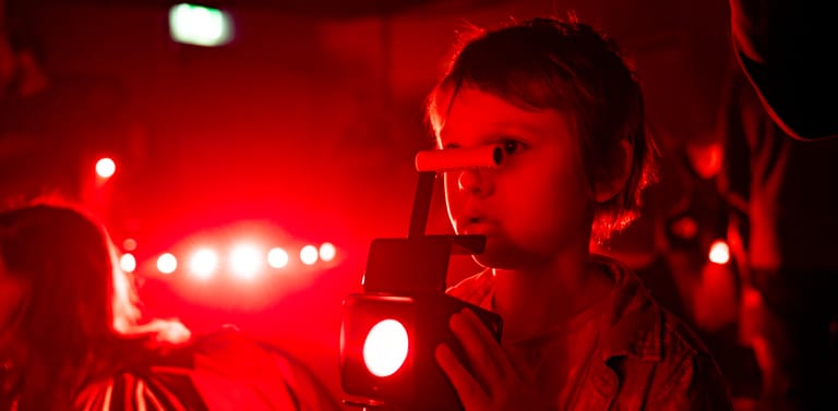 Person illuminated by intense red stage lighting and bright spotlights in a theatrical performance setting.