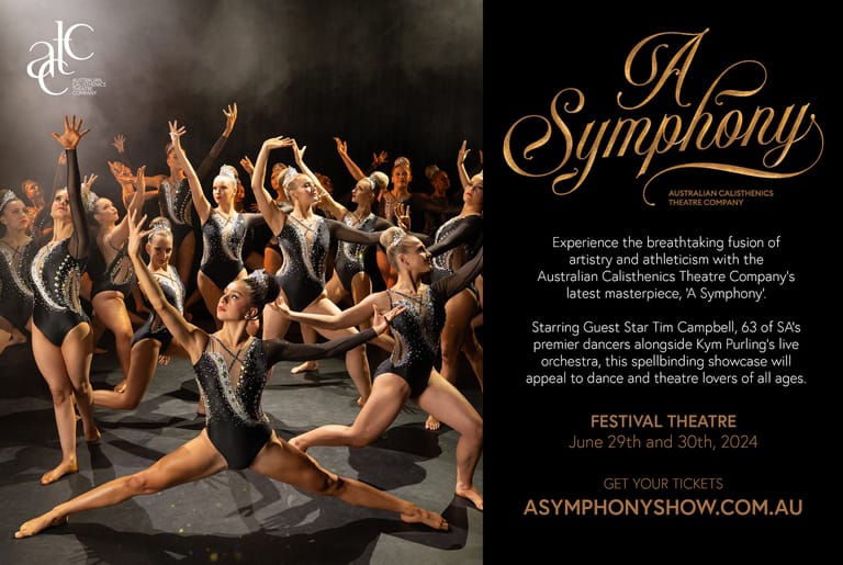 Ensemble of dancers in black attire leap and pose dynamically on stage, lit by warm amber lighting.