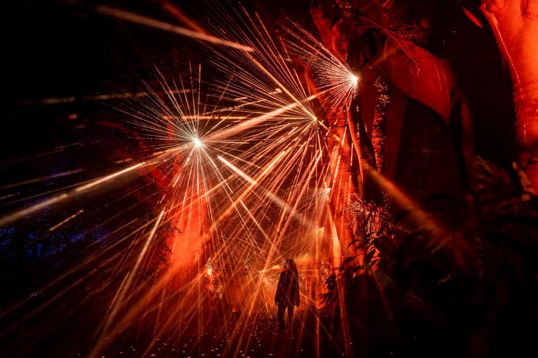 Bright orange and yellow sparks burst outward against a dark background in an abstract explosion of light.