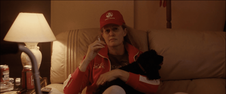 Person in red cap and jacket sitting on a couch with a black dog under warm lamp lighting.