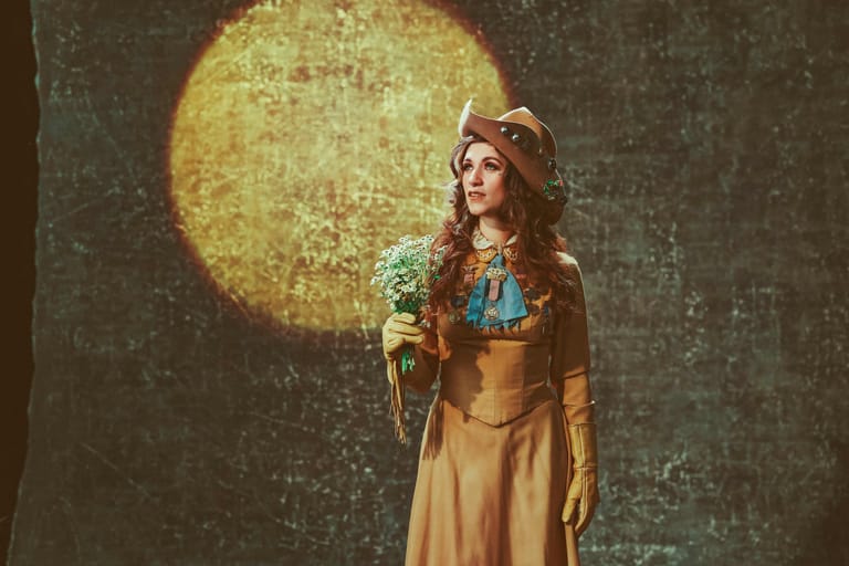 Performer in vintage dress holds microphone against a glowing yellow moon backdrop.