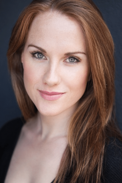Woman with long auburn hair against a dark blue background, looking directly at camera.