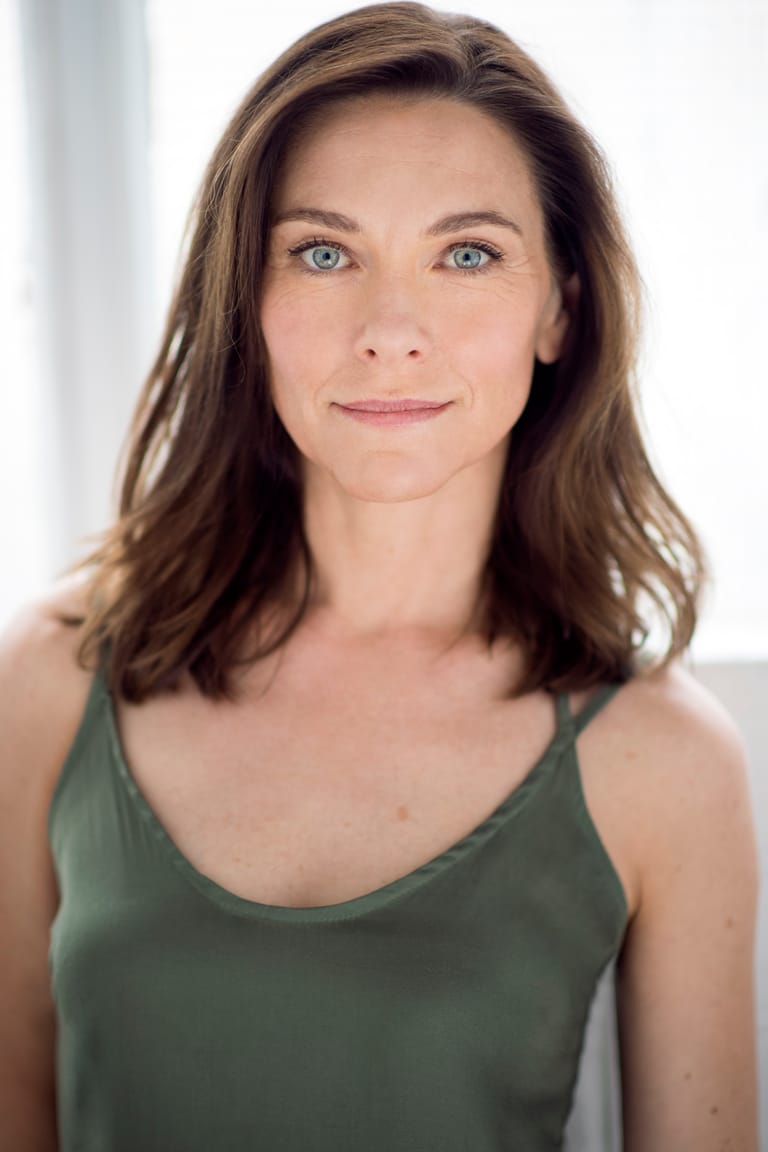 Woman with shoulder-length brown hair wearing a sage green sleeveless top, against a neutral white background.