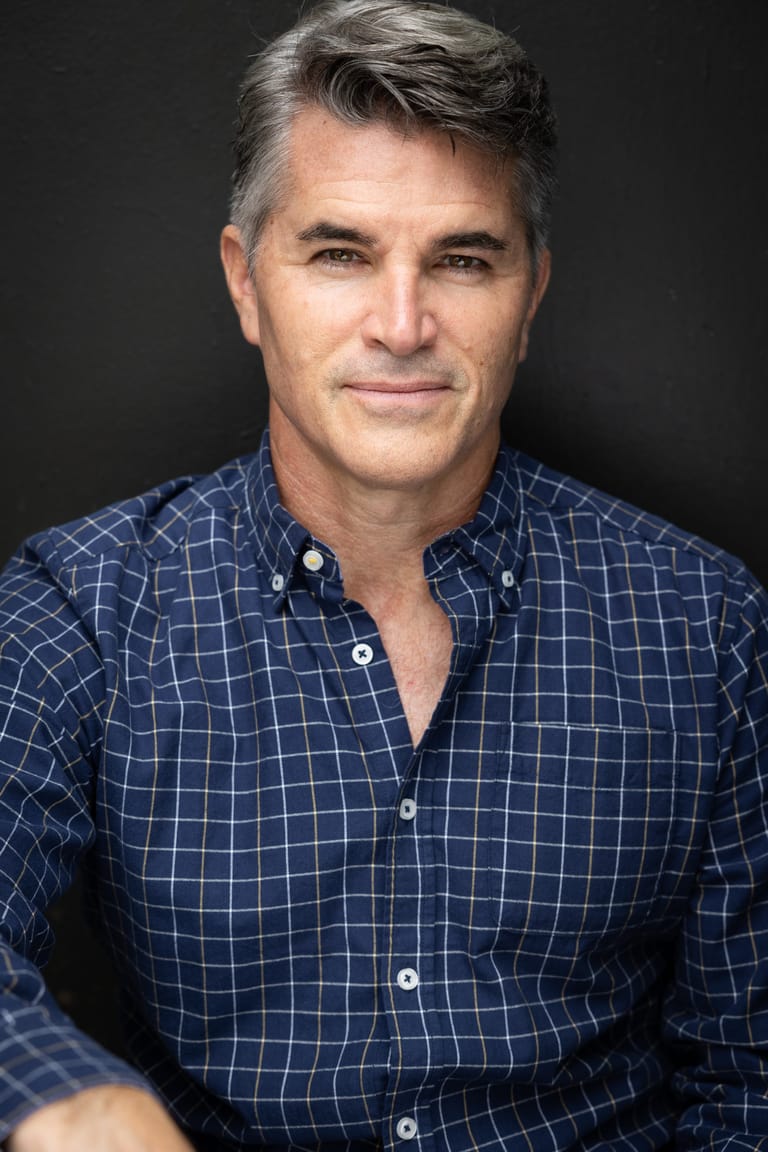 Man in navy checkered shirt against dark background, professional headshot style portrait.