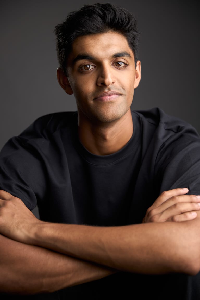 Man in a dark t-shirt with arms crossed against a neutral grey background.