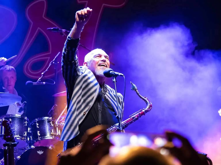 Performer raises fist triumphantly on stage amid purple lighting and stage smoke.