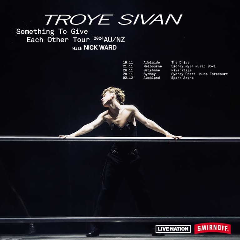 Shirtless performer stretches across a horizontal bar in dramatic stage lighting during a concert tour promotion.