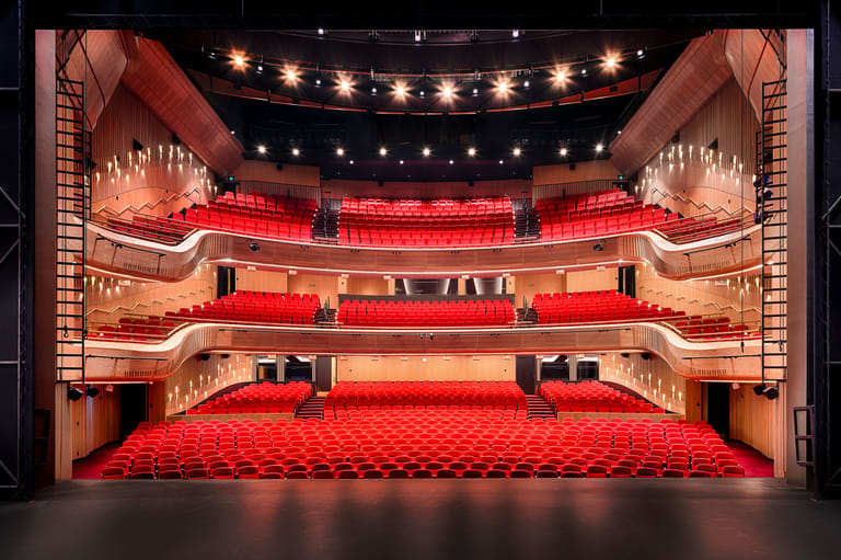 Ornate theatre interior with red velvet seats and balconies, empty and lit by warm overhead lights.