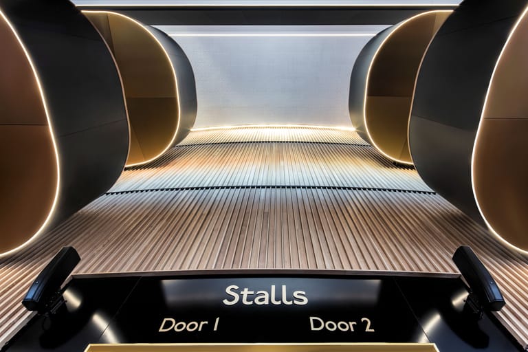 Symmetrical view down a theatre stalls corridor with curved architectural elements and illuminated signage indicating door access.