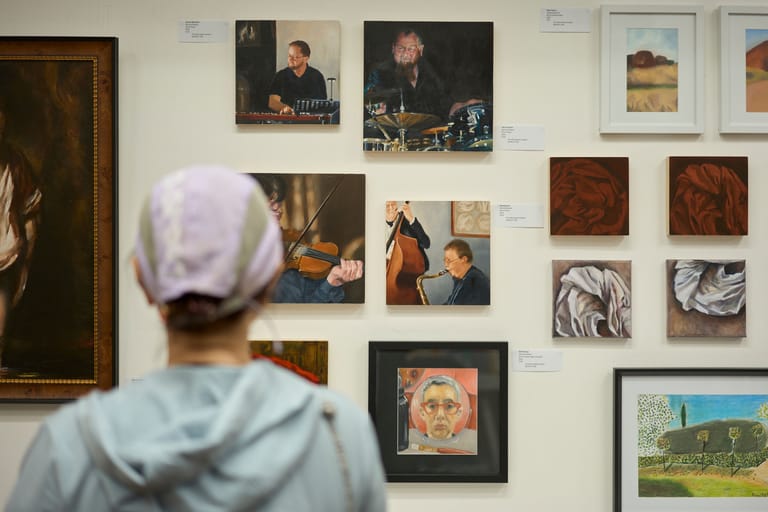 Visitor viewed from behind studying a gallery wall displaying framed portraits and artworks.