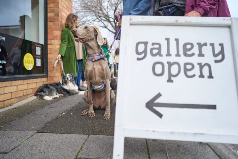 Gallery open" sign directs visitors toward a brick building entrance where a woman and child stand beside a large dog.