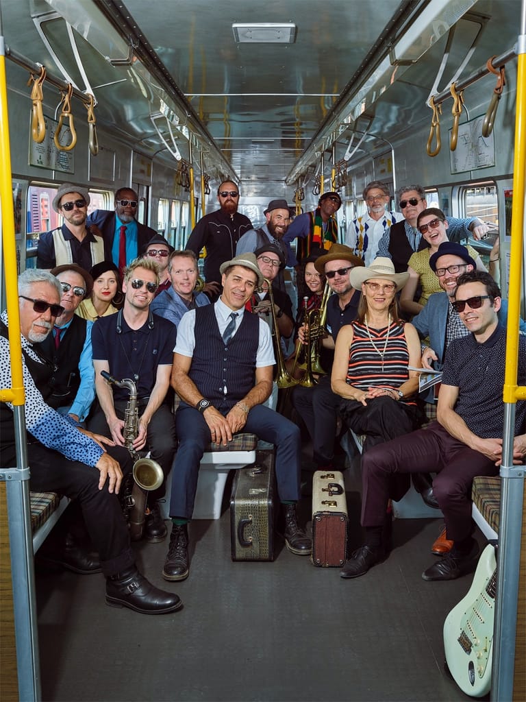 Large group of musicians and performers posing inside a tram, holding instruments and suitcases.