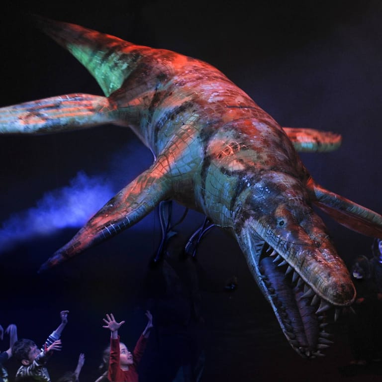Bioluminescent sea creature projection looms above silhouetted audience members in darkness.