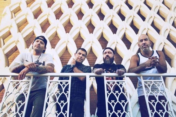 Five men stand on a decorative balcony against a geometric patterned building facade.