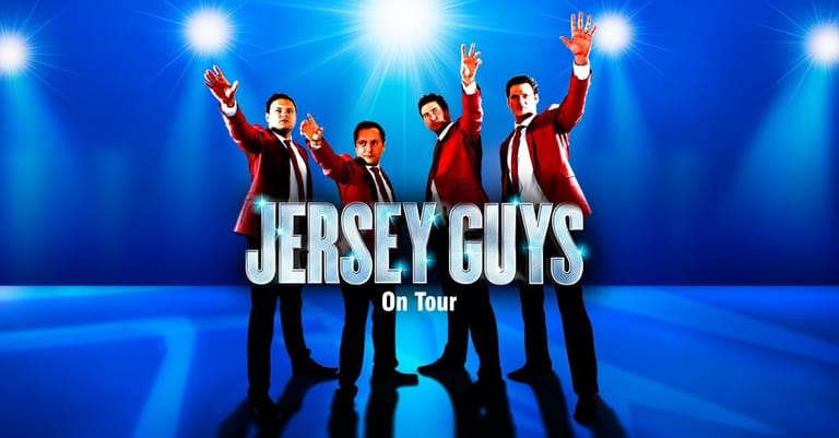 Five performers in burgundy jackets raise their arms on a blue-lit stage with "Jersey Guys On Tour" text displayed.