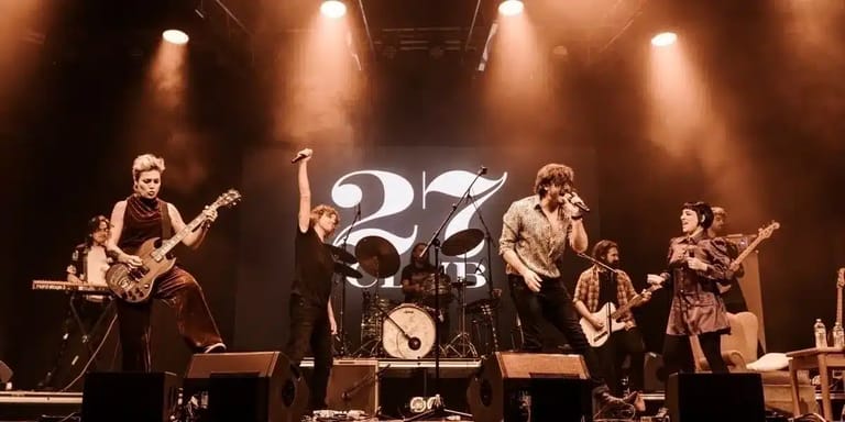 Five-piece band performing on stage with warm spotlighting and large "127" logo backdrop.
