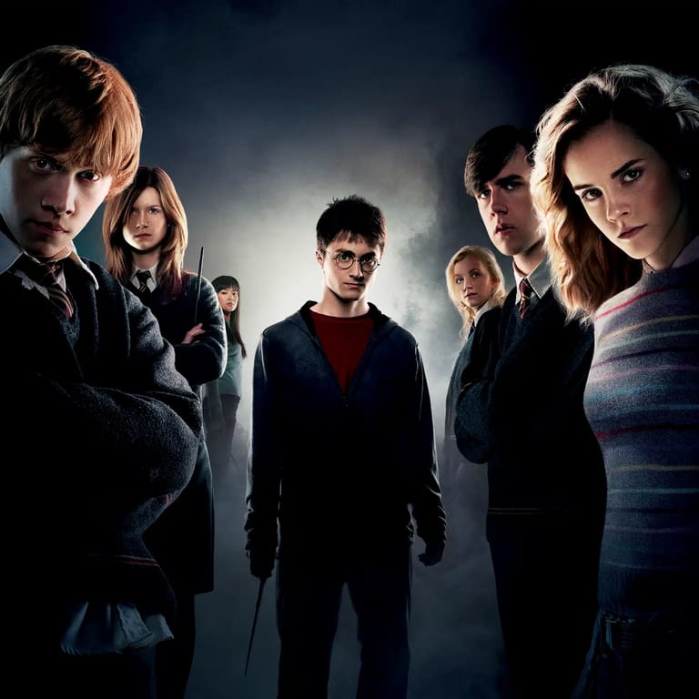 Seven young people in school uniforms stand in dramatic lighting against a dark background.