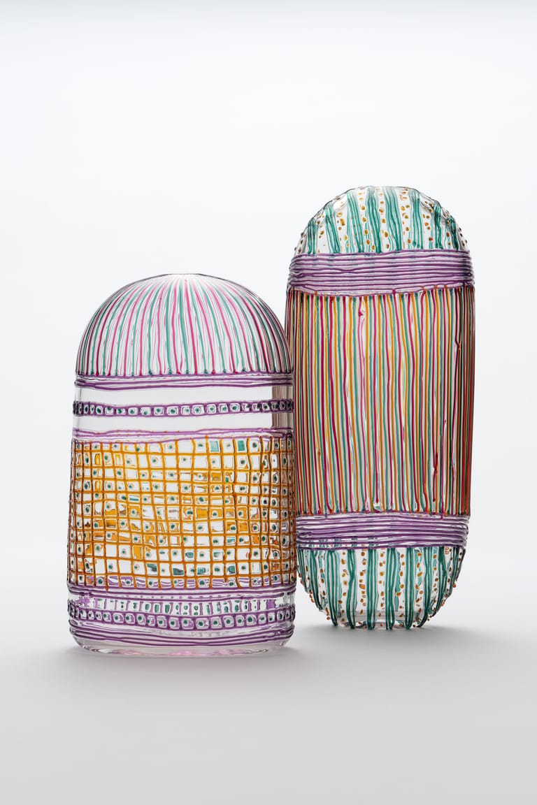 Two glass vessels with colourful striped and patterned wrapping in pink, green, yellow and purple tones against a white background.