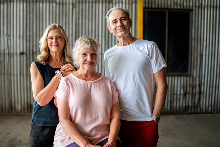 Three people stand together in front of a corrugated metal wall in an industrial space.