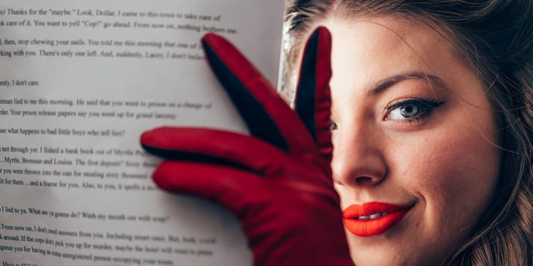 Woman with red lipstick and red gloves posed against text, gazing toward camera with dramatic lighting.